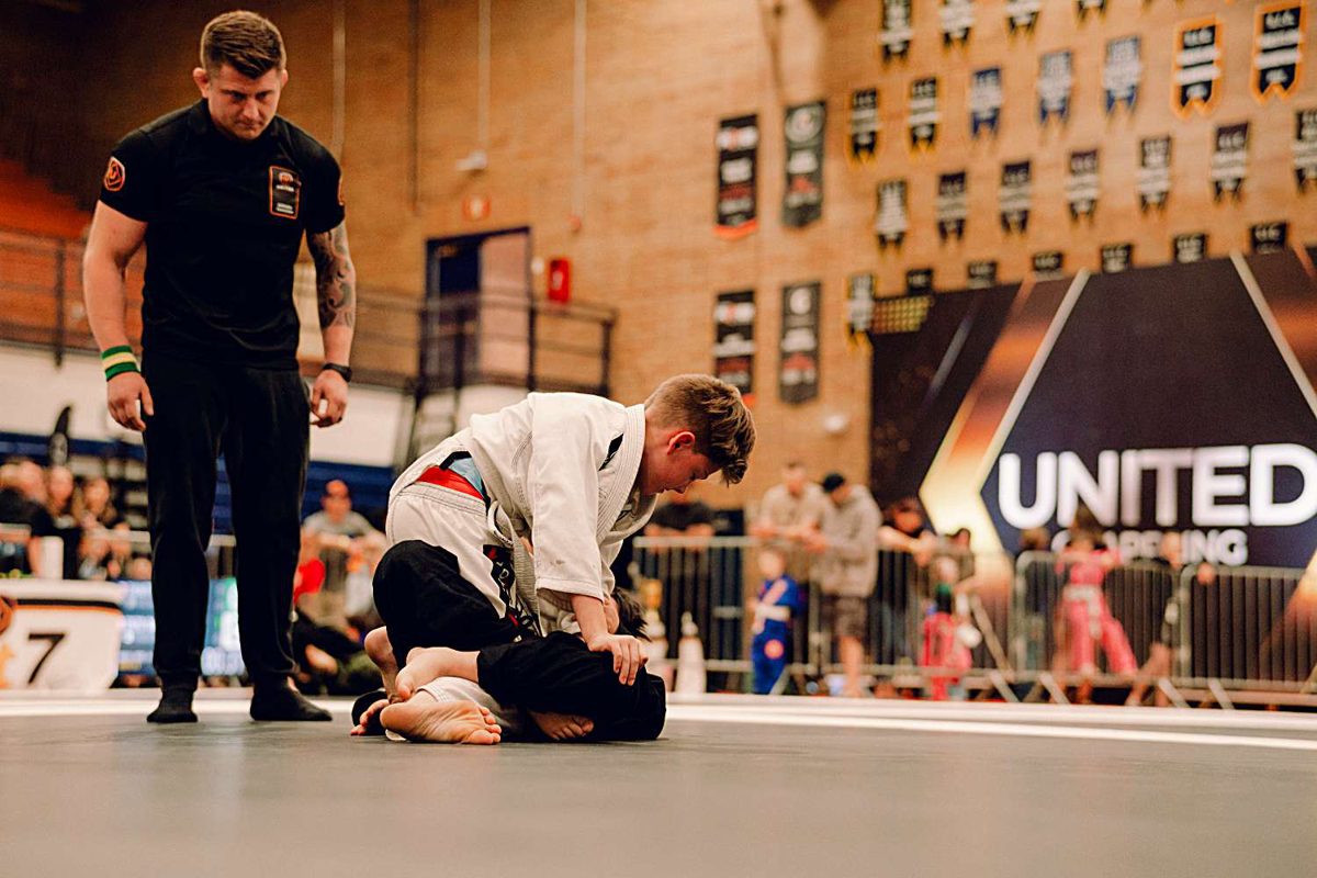 Referee watching a guard pass under the United Grappling banner